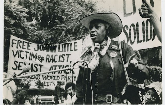 A black and white photograph of Kennedy, center, at a protest rally in support of Joann Little, a young African American accused of murdering her jailor-rapist in 1974.