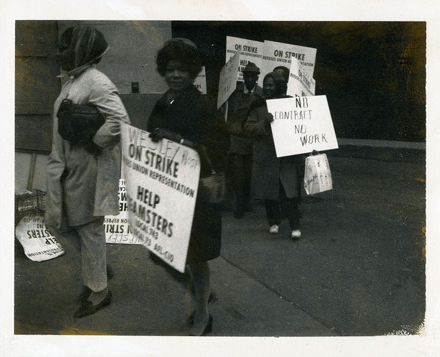 A black and white photograph of Wyatt holding a sign and smiling at the camera while walking the Wesley Hospital picket line with others, 1970s. Photo source: Chicago Public Library, Vivian G. Harsh R