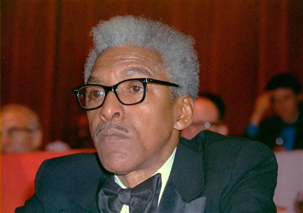 A color photograph of Rustin, depicted later in life, wearing a tuxedo and glasses while sitting in a theatre in New York in 1970. Photo Source: WHYY Media.