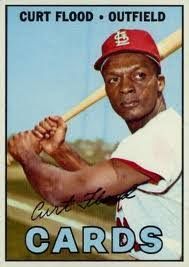 A baseball card with Flood holding a bat, as if about to swing, with his signature and the words “Curt Flood: Outsider” on the top and “Cards” at the bottom. Photo Source: Society for American Basebal