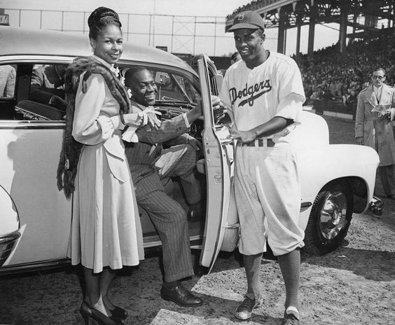 Brooklyn Dodgers baseball player Jackie Robinson (right) receives the keys to a car from tap dancer Bill “Bojangles” Robinson (center) as Jackie Robinson's wife, Rachel (left), looks on at Ebbets