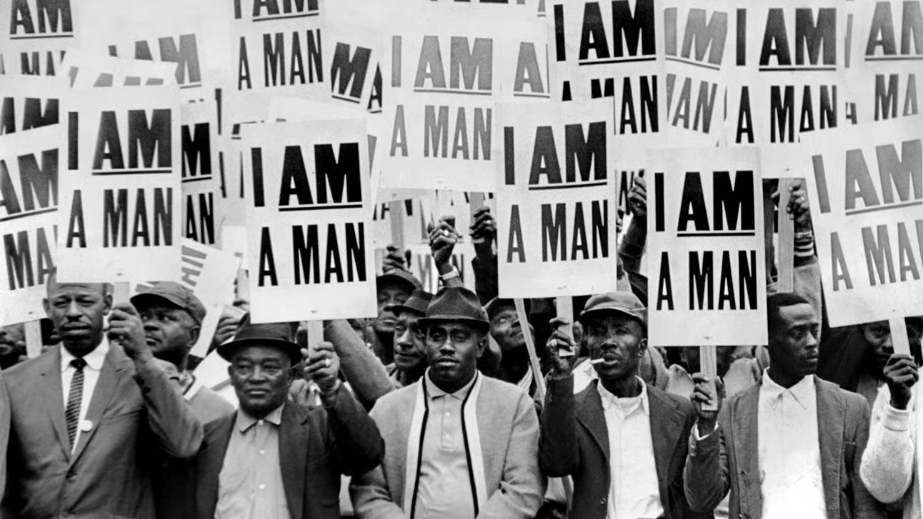 This iconic black and white photograph from the 1968 Memphis Sanitation Workers' Strike shows a group of African American men holding protest signs that read "I AM A MAN. Photo Source: Libra