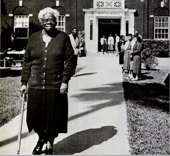 A black and white photograph of Mary McLeod Bethune standing in front of White Hall, a building on the campus of her school Bethune-Cookman College (now University), Daytona Beach, Florida in 1955. Ph