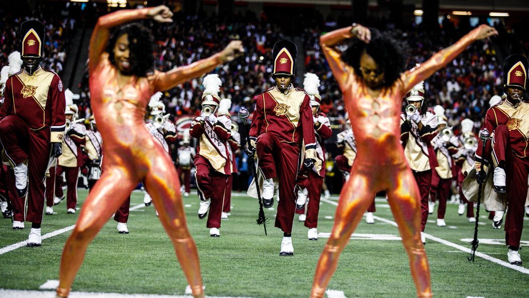 A photograph of Bethune-Cookman University "14 Karat Gold" dancers alongside their marching band performing on the field at homecoming. Photo Source: NYTimes.