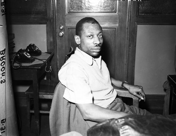 A black and white photograph of Tappes seated in pants and a polo, looking at the camera. Photo Source: The Reuther Library