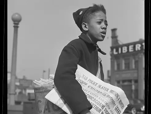 A young newsboy sells papers on a Chicago street corner in the 1940s
